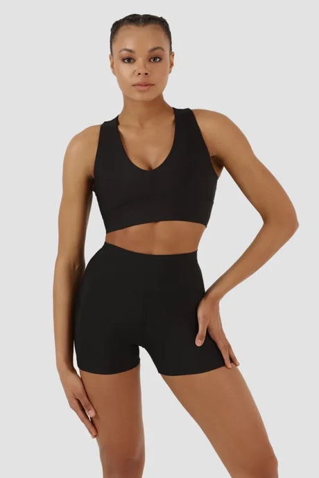 Woman wearing a black sports bra and shorts set on a light grey background