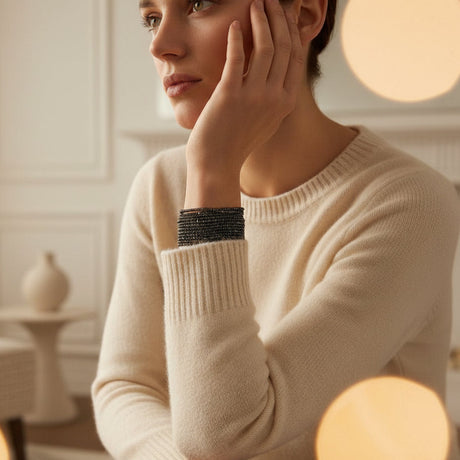 Woman wearing a beige sweater with a black bracelet on her arm in a softly lit room