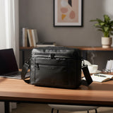 Black crossbody bag on a wooden desk with a laptop and books in the background