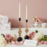 Two black and gold holders with white tapers beside floral wrapped gift boxes