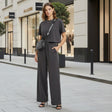 Woman in a grey outfit standing on a city street with shops in the background