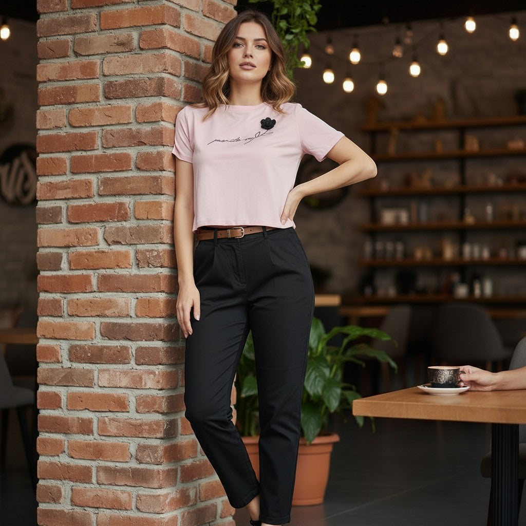 Woman in a pink shirt and black pants leaning against a brick wall in a cozy indoor setting
