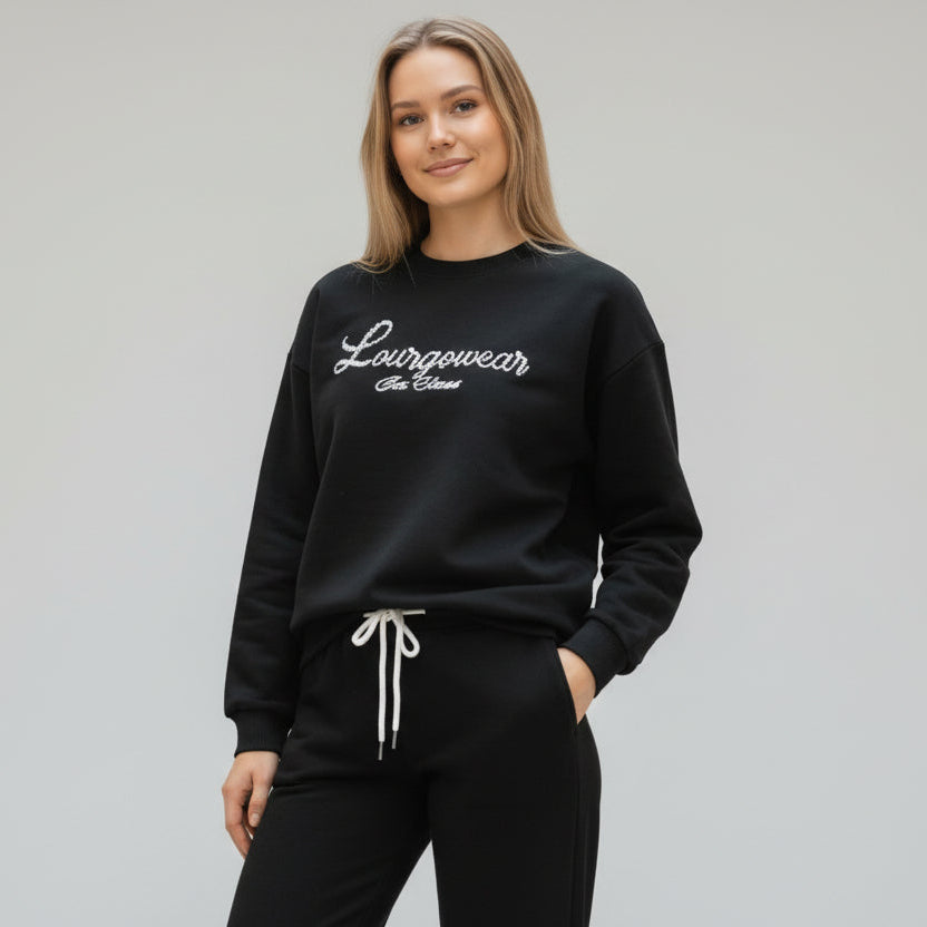 Woman wearing a black sweatshirt with 'Loungewear' text, and black sweatpants on a grey background