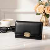 Black wallet with gold clasp on a surface with sunglasses, coffee, and flowers in the background