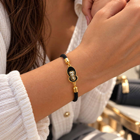 Wrist wearing a black cord bracelet with a gold edged black enamel charm and a cream motif