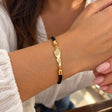 Wrist wearing a black braided cord bracelet with a textured gold Lebanon map charm