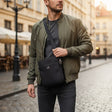 Man holding a black crossbody bag on a city street