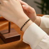 Black beaded tennis bracelet with a gold clasp worn by a person