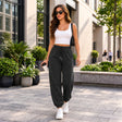 Woman holding a coffee in black cuffed joggers with a drawstring waist, a white tank top and white sneakers
