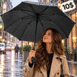 Woman in a trench coat holding an open black umbrella with a curved grip on a rainy street