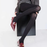 Person wearing black design collant and maroon shoes sitting on a white surface