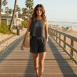 Woman wearing a black outfit, walking on a wooden boardwalk by the beach with palm trees and ocean view