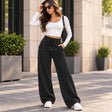 Woman in black wide leg sweatpants with an elastic waist and drawstring, a white crop top and white sneakers