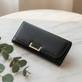 Black wallet with a gold clasp on a marble surface with leaves