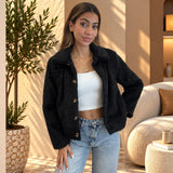 Black cropped faux fur jacket worn open over a white crop top, one hand on hip