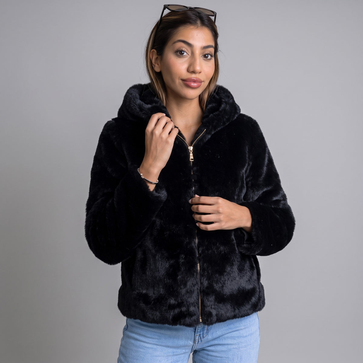 Black plush faux fur hooded jacket with a gold zip worn open over light blue jeans