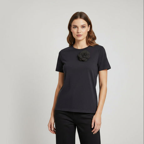Woman wearing a black tshirt with a black flower accessory on a light gray background
