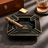 Cigar, gold lighter and whiskey arranged around the black square ashtray on wood