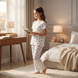 Girl in a white pajama set with black heart print reading a book