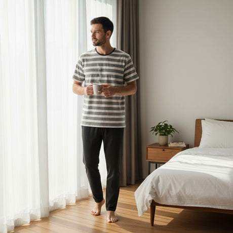 Black heather pyjama set worn holding a mug by a bedroom window