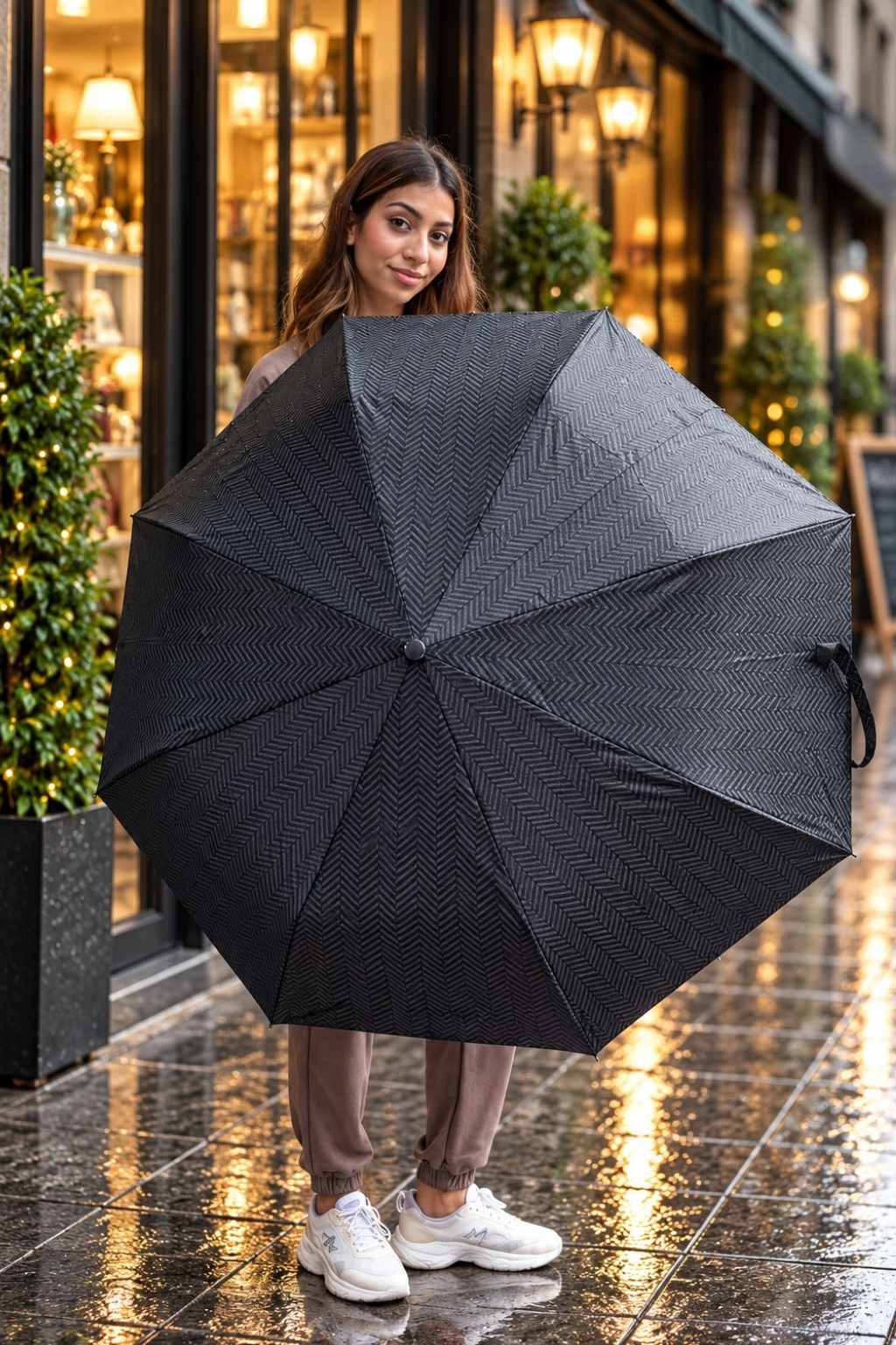 Woman holding open a black herringbone folding umbrella outside a lit shop window