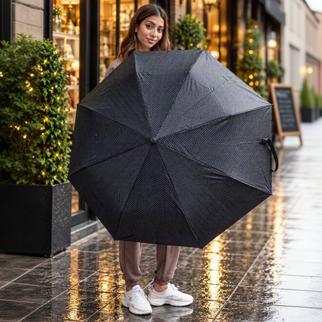 Woman holding open a black herringbone folding umbrella outside a lit shop window
