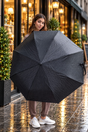 Woman holding open a black herringbone folding umbrella outside a lit shop window