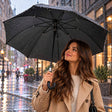 Woman holding a black umbrella with a J hook handle and silver collar under falling rain