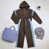 Black hoodie and wide leg pants with light blue stripes laid flat beside a quilted tote