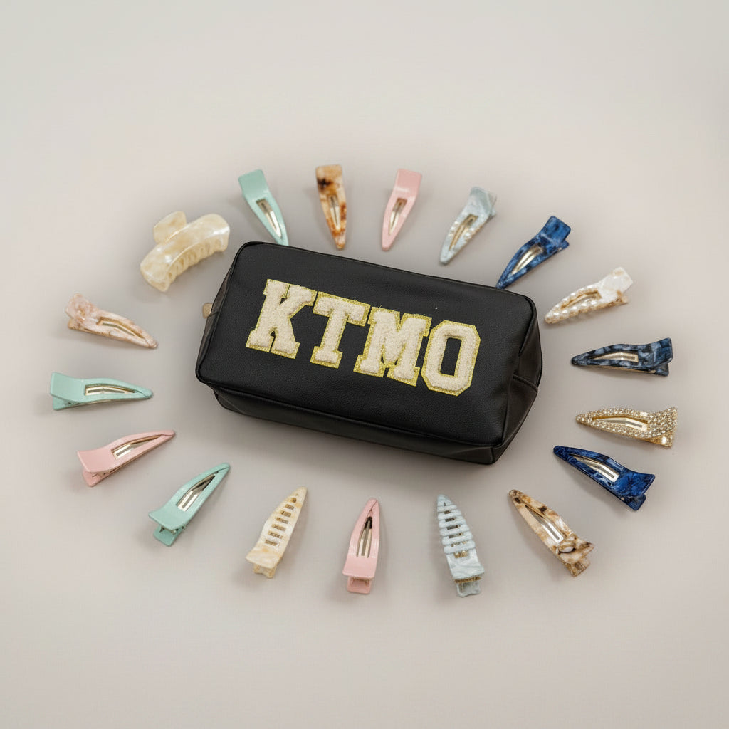 Black pouch with 'KTMO' text surrounded by various hair clips on a light grey background