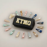 Black pouch with 'KTMO' text surrounded by various hair clips on a light grey background