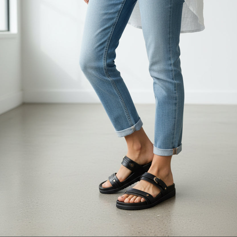 Person wearing black sandals and light blue jeans on a plain floor.