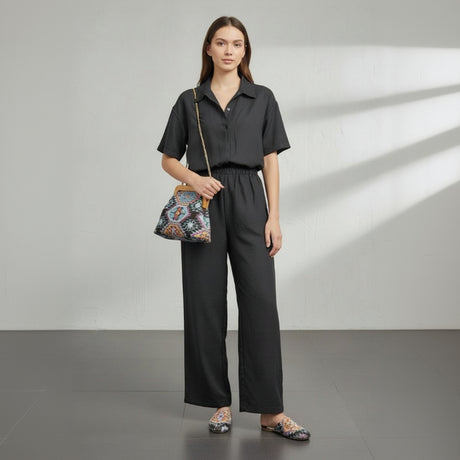 Woman in black outfit holding a patterned handbag against a neutral background