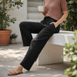 Person sitting outdoors holding a cup, wearing a brown top and black linen pants