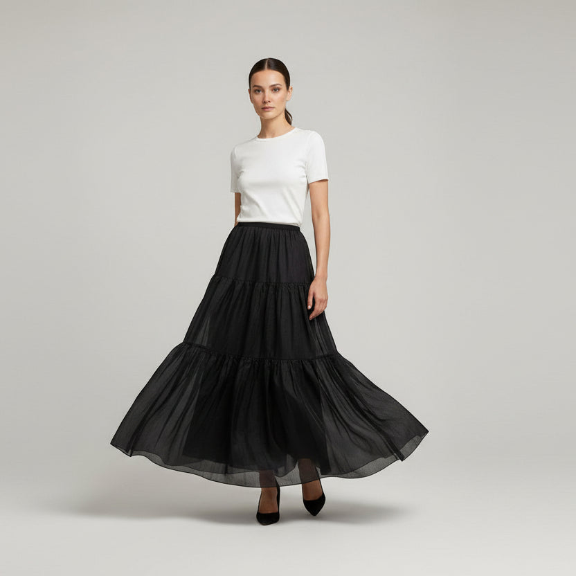 Woman wearing a black tiered skirt and white top on a light gray background