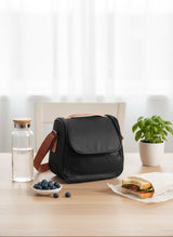 Black bag on a table with a water bottle, bowl of blueberries, and sandwich