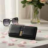 Black wallet with gold accent on a surface with sunglasses and flowers in the background