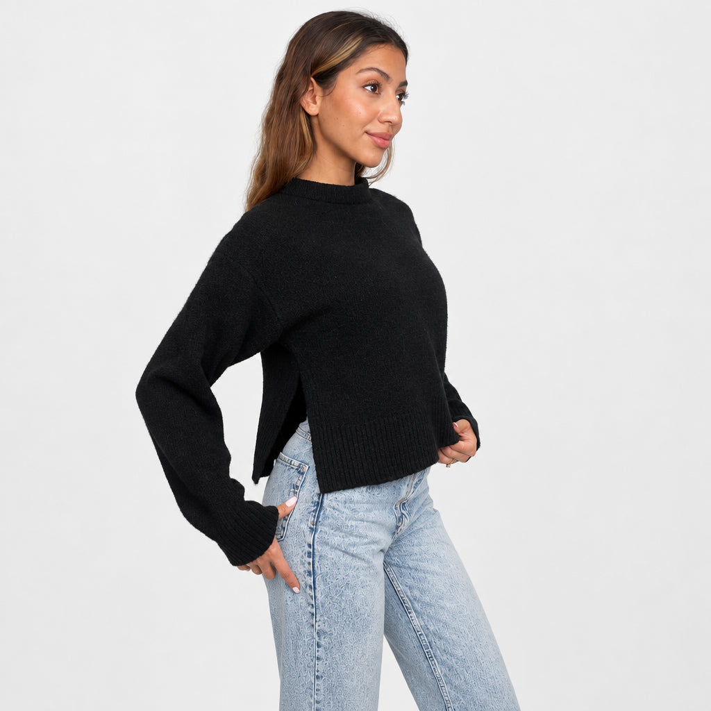 Side view of a black cropped sweater with long sleeves and ribbed cuffs