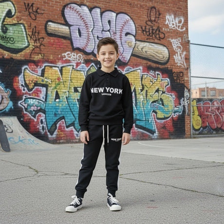 Boy in a black New York collared sweatshirt and joggers standing by a graffiti wall