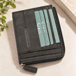 Teal cards peek from the outer slots of a flat black nubuck wallet with a zip pull
