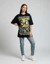 Person wearing a black graphic tshirt with a yellow duck graphic and ripped jeans on a plain background