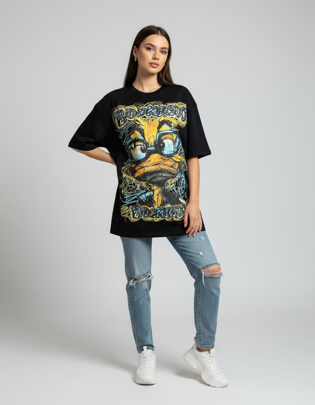 Person wearing a black graphic tshirt with a yellow duck graphic and ripped jeans on a plain background