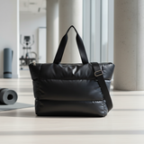Black puffer bag on a light wooden floor with a blurred indoor background