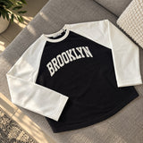 Black Brooklyn sweatshirt with white raglan sleeves laid flat on a grey sofa