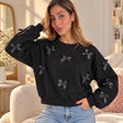 Woman in a black cropped sweatshirt covered in black satin bows, hand in her hair