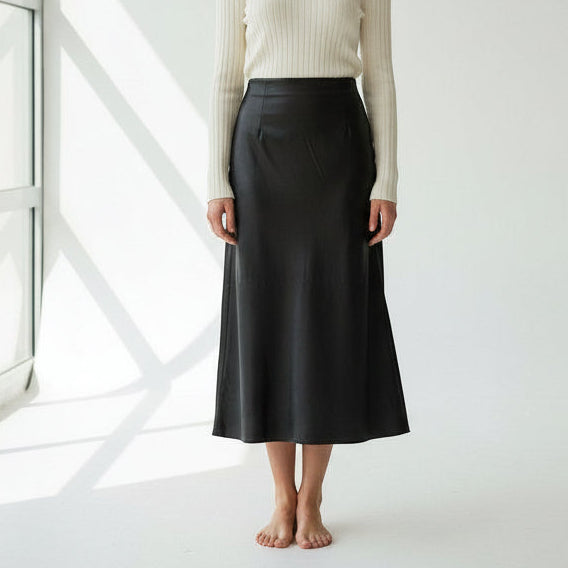 Person wearing a black skirt and cream sweater in a minimalistic setting