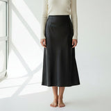 Person wearing a black skirt and cream sweater in a minimalistic setting