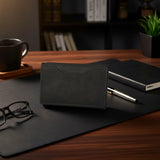 Black leather wallet, glasses, and pen on a wooden desk with a blurred background