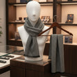 Mannequin wearing a black and grey scarf with a matching hanged scarf in a store setting