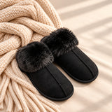 Pair of black suede look slippers with black faux fur cuffs on a knit throw
